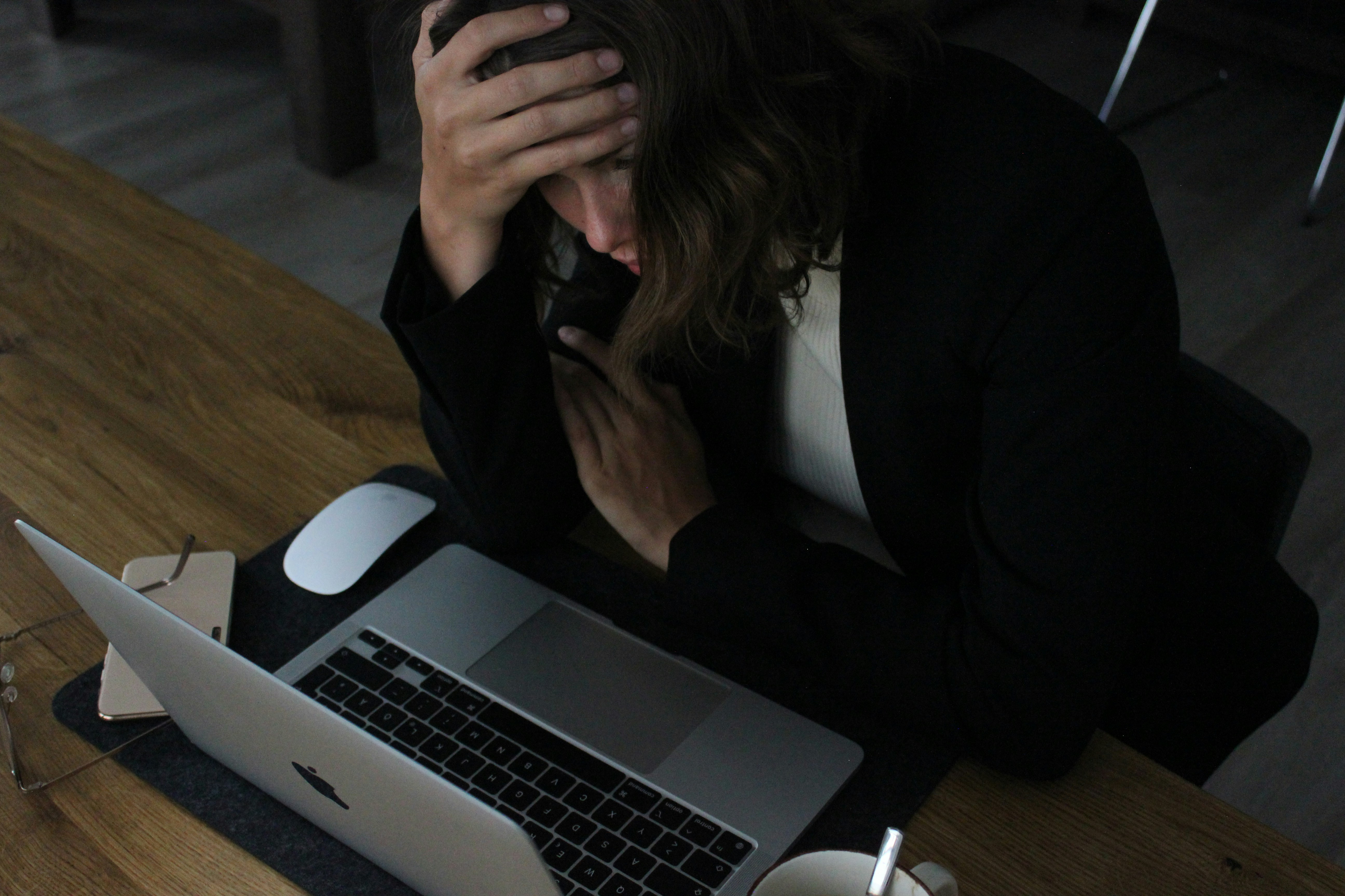 A woman with her head in her hands, sitting behind a laptop